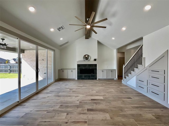 unfurnished living room featuring ceiling fan, light hardwood / wood-style floors, beam ceiling, and a tiled fireplace