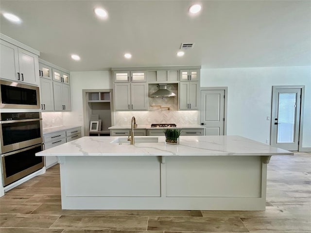 kitchen featuring light stone countertops, appliances with stainless steel finishes, wall chimney exhaust hood, and a spacious island