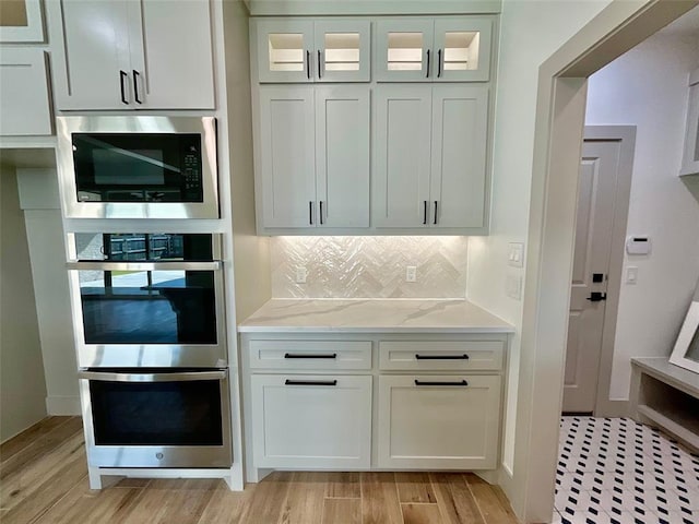 kitchen featuring white cabinets, light stone counters, light wood-type flooring, and stainless steel appliances