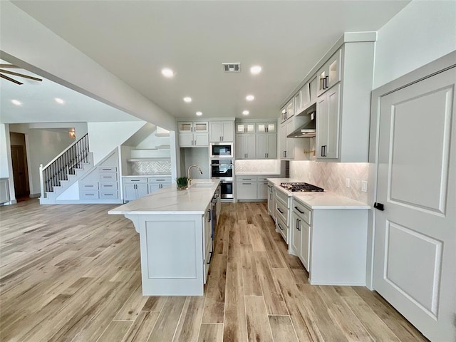 kitchen featuring decorative backsplash, light wood-type flooring, stainless steel appliances, a kitchen island with sink, and sink