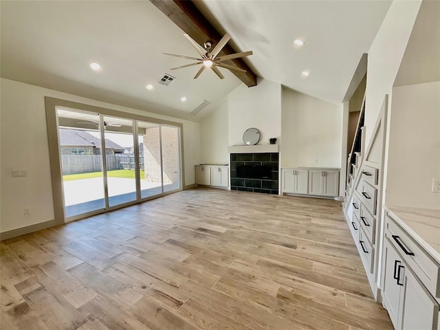 unfurnished living room featuring a tile fireplace, ceiling fan, beamed ceiling, and light wood-type flooring