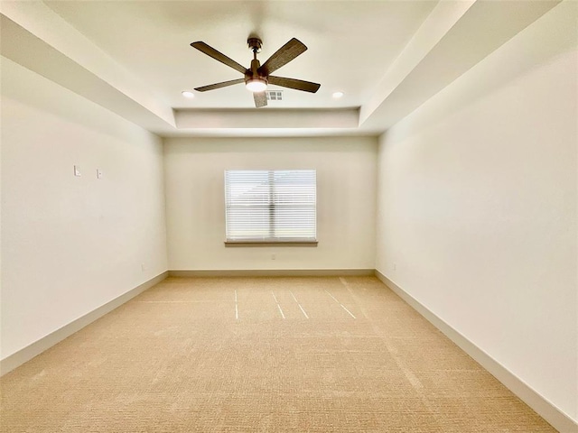 carpeted spare room featuring a tray ceiling and ceiling fan