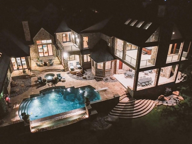 pool at night featuring an in ground hot tub and a patio area