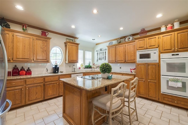 kitchen with light stone countertops, a center island, a kitchen breakfast bar, white appliances, and decorative backsplash