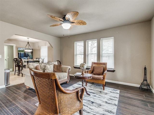 living room featuring dark wood-type flooring, baseboards, arched walkways, and ceiling fan