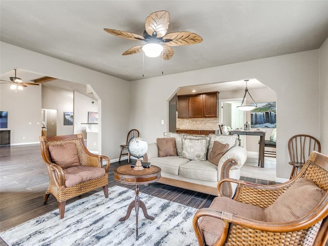 living area featuring baseboards, light wood-type flooring, vaulted ceiling, arched walkways, and a ceiling fan