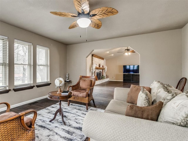 living area featuring a fireplace, dark wood finished floors, a ceiling fan, and vaulted ceiling