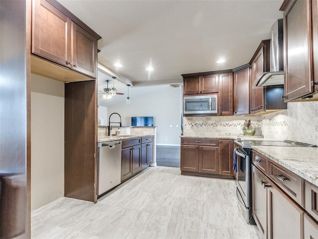 kitchen with decorative backsplash, appliances with stainless steel finishes, wall chimney exhaust hood, and a sink