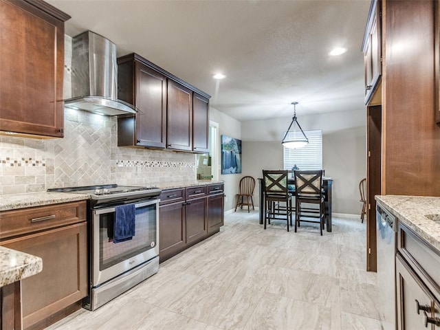 kitchen featuring backsplash, light stone countertops, hanging light fixtures, stainless steel appliances, and wall chimney exhaust hood