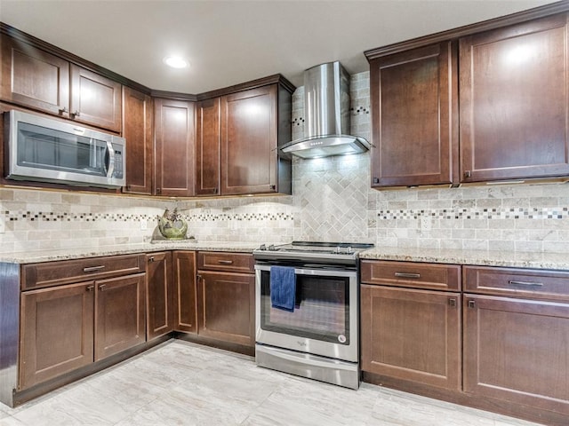 kitchen featuring backsplash, stainless steel appliances, wall chimney exhaust hood, and light stone countertops