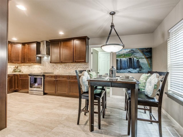 kitchen with baseboards, wall chimney range hood, light countertops, decorative backsplash, and stainless steel range