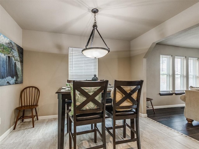 dining space featuring baseboards, arched walkways, and wood finished floors