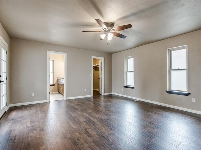 unfurnished bedroom with dark wood-style floors, a spacious closet, a textured ceiling, and baseboards