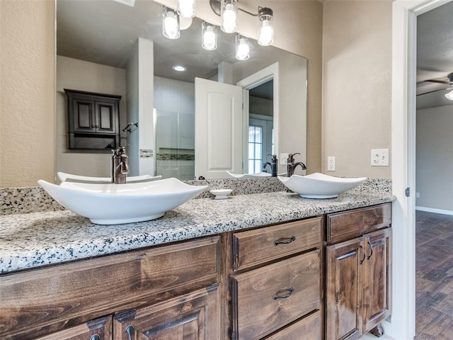 bathroom featuring a shower stall, wood finished floors, double vanity, and a sink