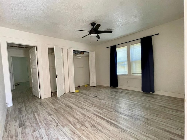 unfurnished bedroom with hardwood / wood-style floors, ceiling fan, a textured ceiling, and two closets