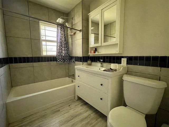 full bathroom featuring hardwood / wood-style floors, vanity, tiled shower / bath, toilet, and tile walls