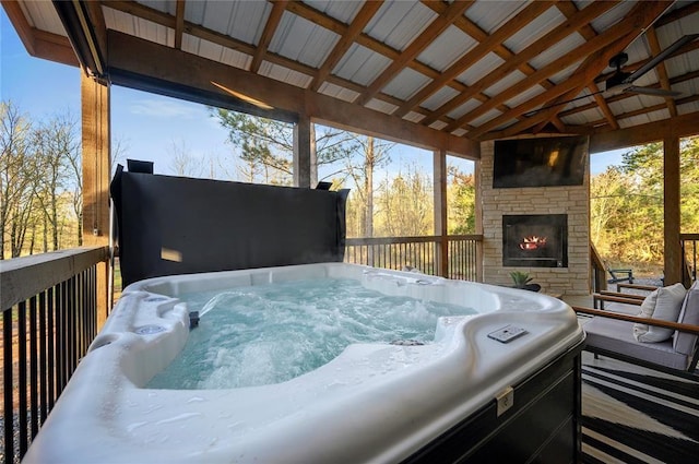 wooden deck featuring an outdoor stone fireplace, ceiling fan, and a hot tub