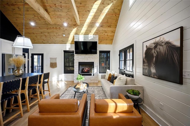 living room with beamed ceiling, light wood-type flooring, a stone fireplace, and a wealth of natural light