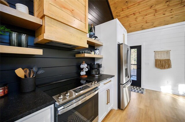 kitchen featuring white cabinets, appliances with stainless steel finishes, light hardwood / wood-style flooring, and wooden walls