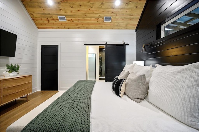 bedroom with vaulted ceiling, a barn door, light hardwood / wood-style flooring, wooden ceiling, and wood walls