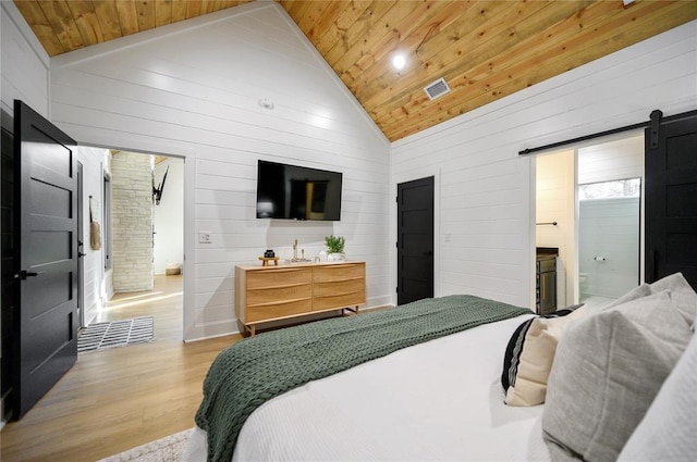 bedroom with connected bathroom, wooden ceiling, a barn door, light hardwood / wood-style flooring, and high vaulted ceiling