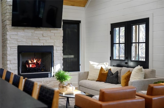 living room featuring vaulted ceiling, a stone fireplace, and wood walls