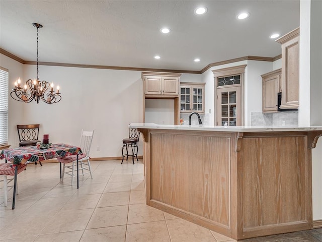 kitchen with an inviting chandelier, hanging light fixtures, crown molding, light brown cabinetry, and a breakfast bar area