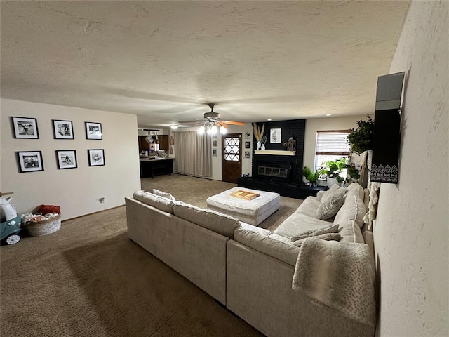 carpeted living room with ceiling fan, a textured ceiling, and a brick fireplace