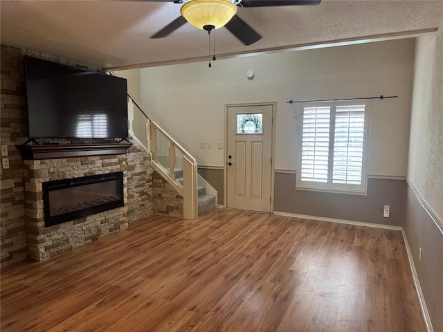 foyer featuring a stone fireplace, hardwood / wood-style flooring, ceiling fan, ornamental molding, and a textured ceiling