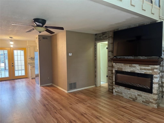 unfurnished living room with a fireplace, light hardwood / wood-style floors, french doors, and ceiling fan