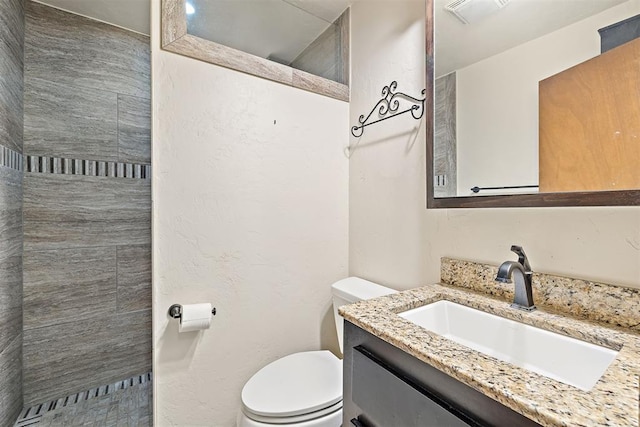 bathroom featuring tiled shower, vanity, and toilet