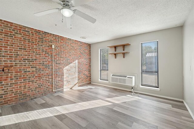 unfurnished room featuring plenty of natural light, light hardwood / wood-style floors, an AC wall unit, and brick wall