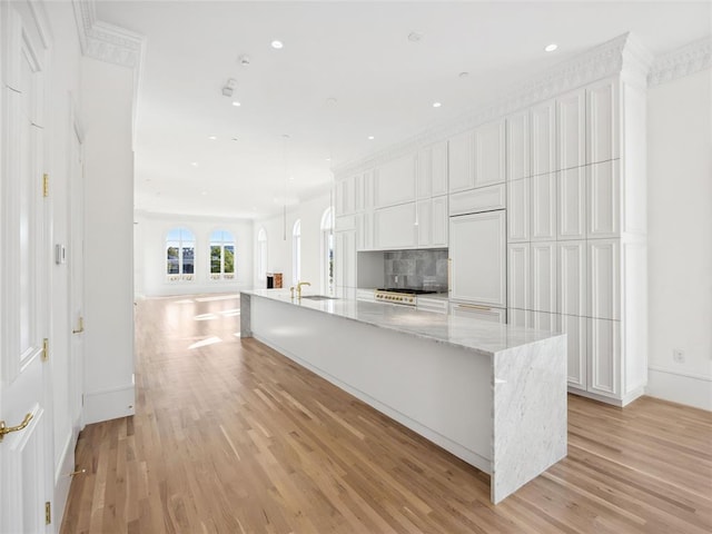 kitchen featuring white cabinets, decorative backsplash, a large island with sink, and light hardwood / wood-style flooring