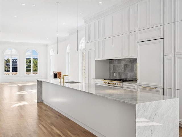 kitchen featuring sink, light stone counters, a large island with sink, crown molding, and white cabinets