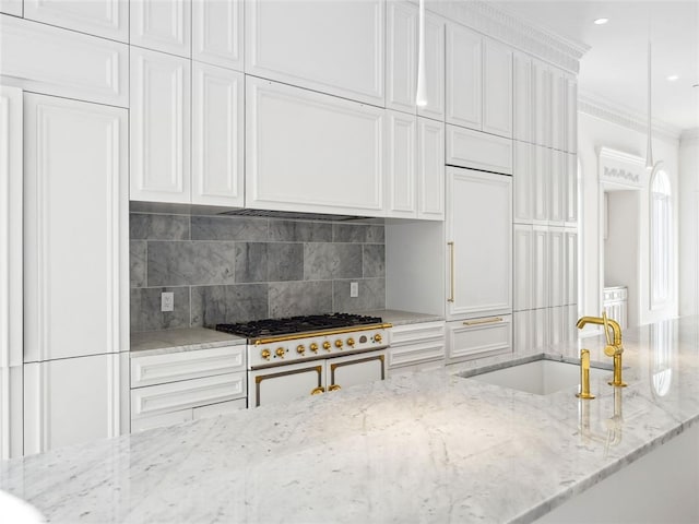 kitchen with light stone countertops, high end stove, white cabinetry, and sink