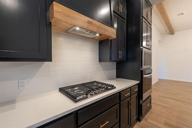 11601 SW 58th St, Mustang, OK 73064 - kitchen featuring appliances with stainless steel finishes, dark cabinetry, tasteful backsplash, light countertops, and beamed ceiling
