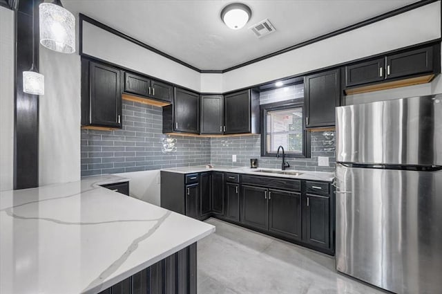 kitchen featuring sink, hanging light fixtures, light stone counters, kitchen peninsula, and stainless steel fridge