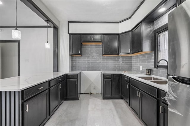 kitchen with stainless steel refrigerator, sink, tasteful backsplash, light stone counters, and pendant lighting