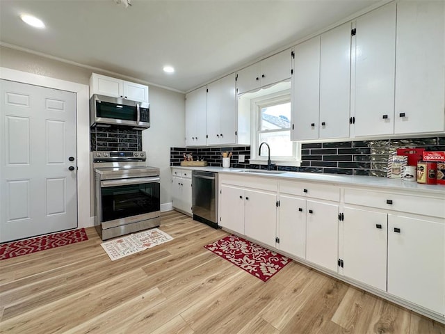 kitchen featuring white cabinetry, sink, stainless steel appliances, backsplash, and light wood-type flooring