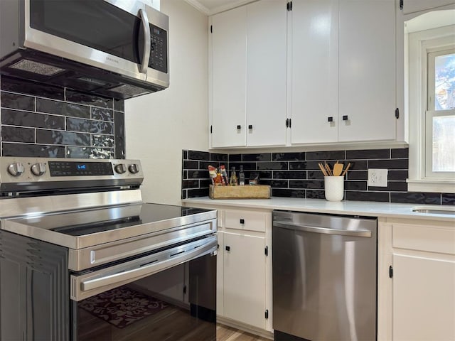 kitchen with decorative backsplash, stainless steel appliances, crown molding, wood-type flooring, and white cabinetry