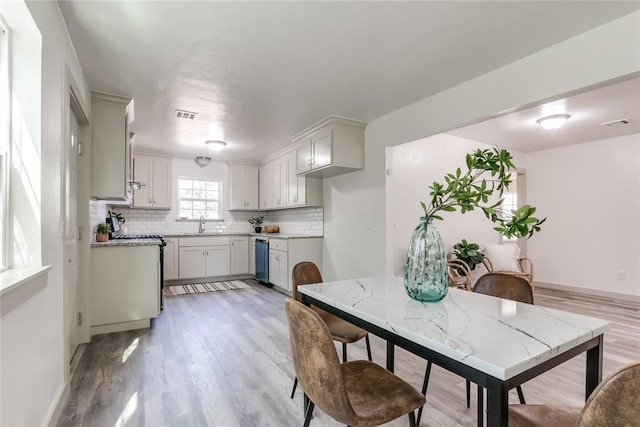 kitchen with backsplash, white cabinetry, dishwasher, and light wood-type flooring