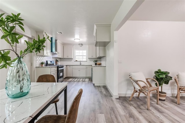 kitchen with decorative backsplash, sink, wall chimney range hood, light hardwood / wood-style floors, and stainless steel range with gas cooktop