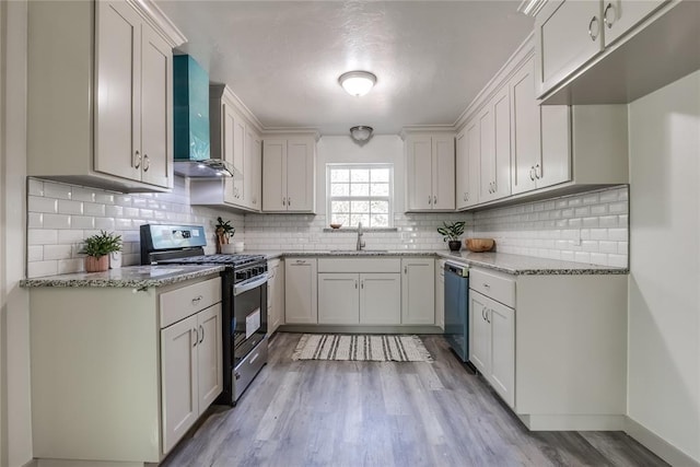 kitchen featuring decorative backsplash, stainless steel appliances, sink, wall chimney range hood, and white cabinetry