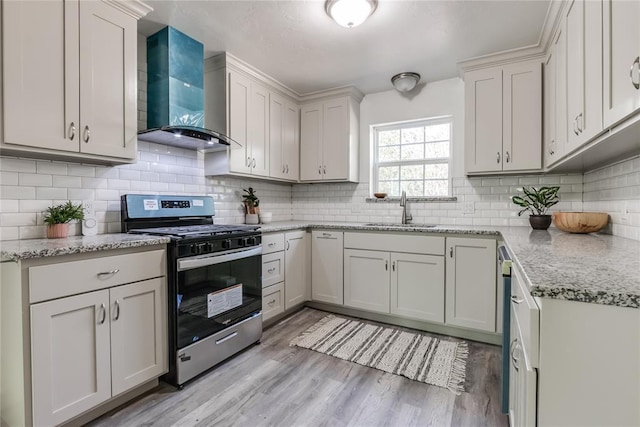 kitchen with gas range, white cabinetry, sink, wall chimney range hood, and light hardwood / wood-style flooring