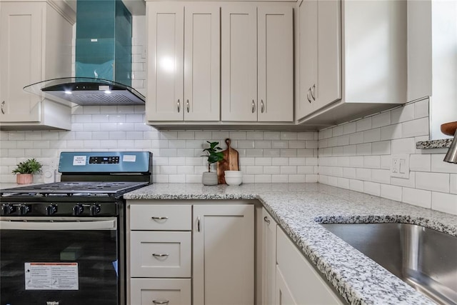 kitchen featuring stainless steel gas range, tasteful backsplash, white cabinets, and wall chimney range hood