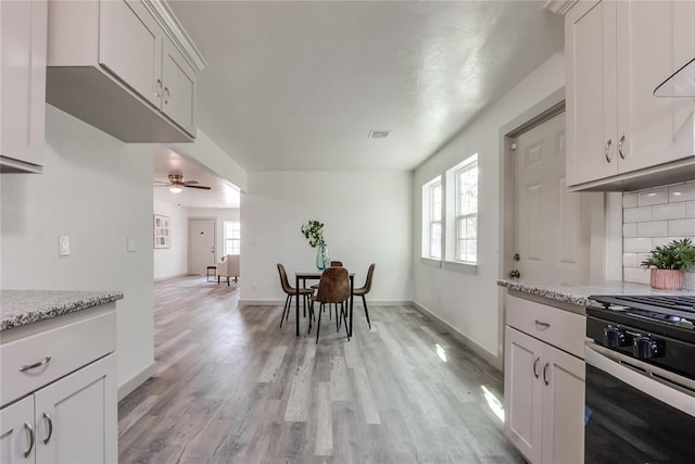 kitchen with white cabinetry, ceiling fan, light stone countertops, light wood-type flooring, and stainless steel range with gas stovetop