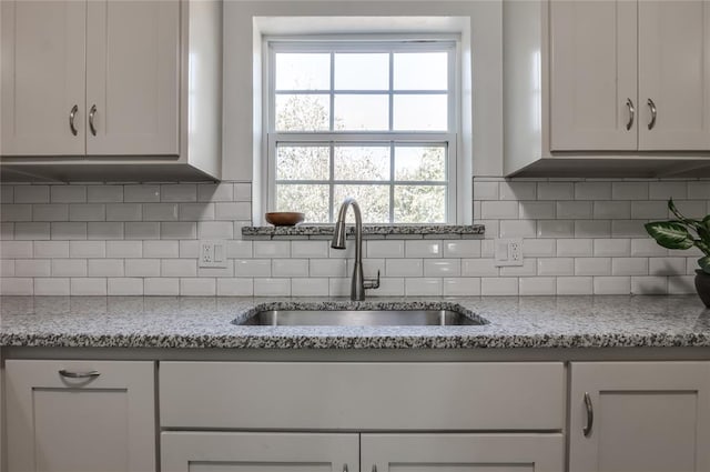 kitchen featuring white cabinets, decorative backsplash, light stone countertops, and sink