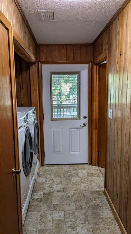 clothes washing area with wooden walls, washer and clothes dryer, and a textured ceiling