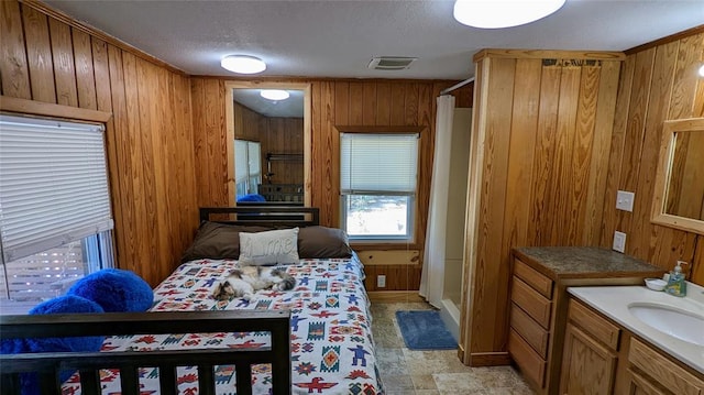 bedroom with a textured ceiling, sink, and wooden walls