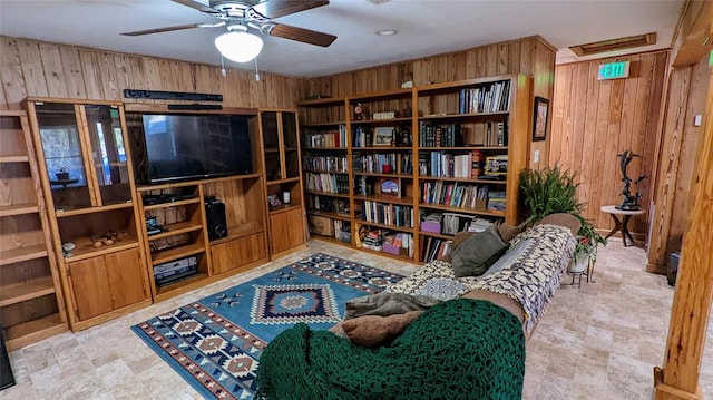 living area with ceiling fan and wooden walls